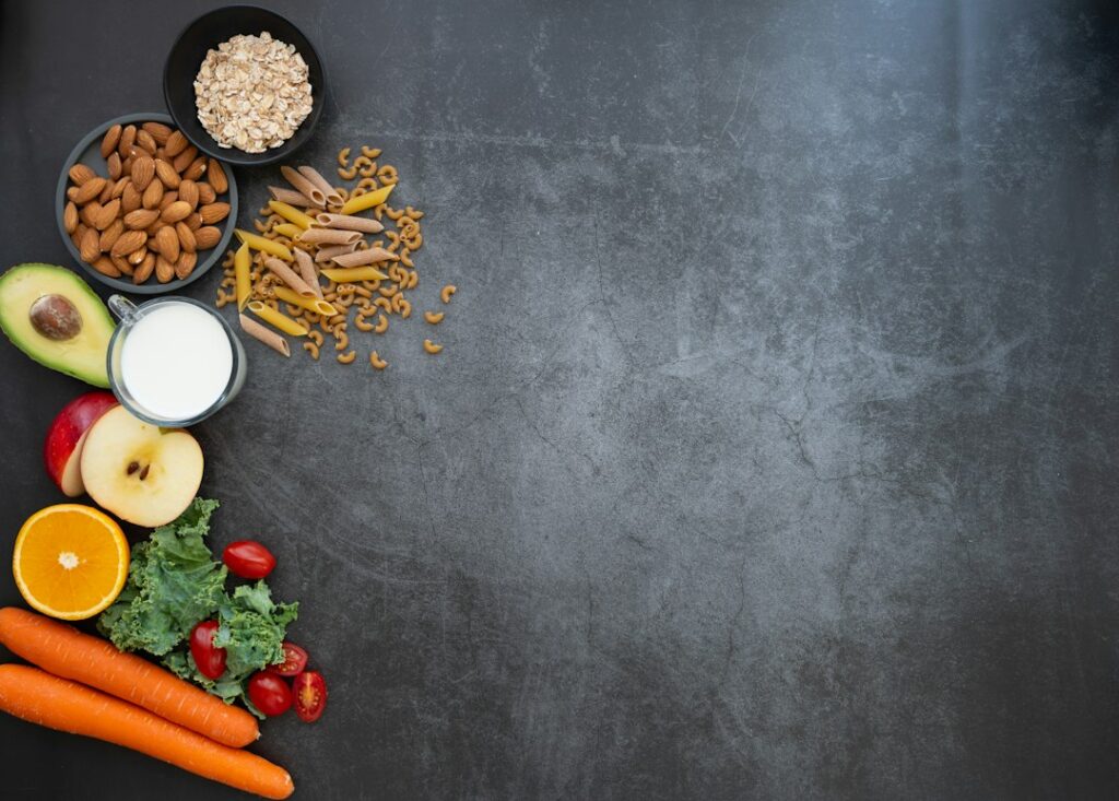 Milk, almonds, pasta and fruit arranged on a grey surface.