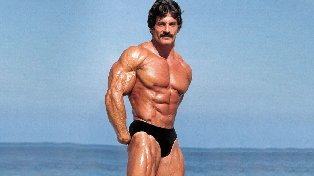 Bodybuilder striking a side pose on the beach.